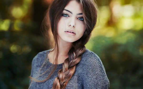 A brunette woman with a braid poses against a soft-focus background in this HD desktop wallpaper, featuring a bokeh effect.