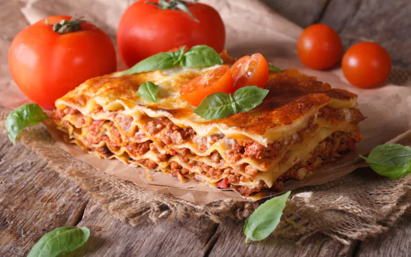 4K Ultra HD wallpaper featuring a close-up of a freshly baked lasagna layered with tomato sauce, pasta sheets, and garnished with basil leaves and ripe tomatoes.