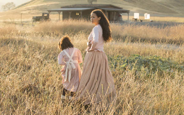 A serene moment from the TV show Westworld featuring Thandie Newton and a child, Jasmyn Rae, walking through a golden grassy field, captured in a stunning HD wallpaper.