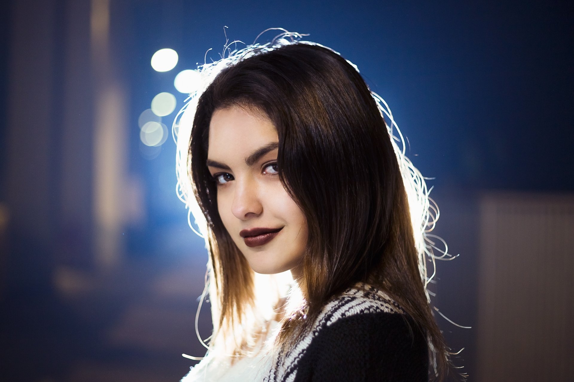 A brunette model with brown eyes and dark lipstick poses confidently against a softly lit background, creating an elegant, high-definition desktop wallpaper.