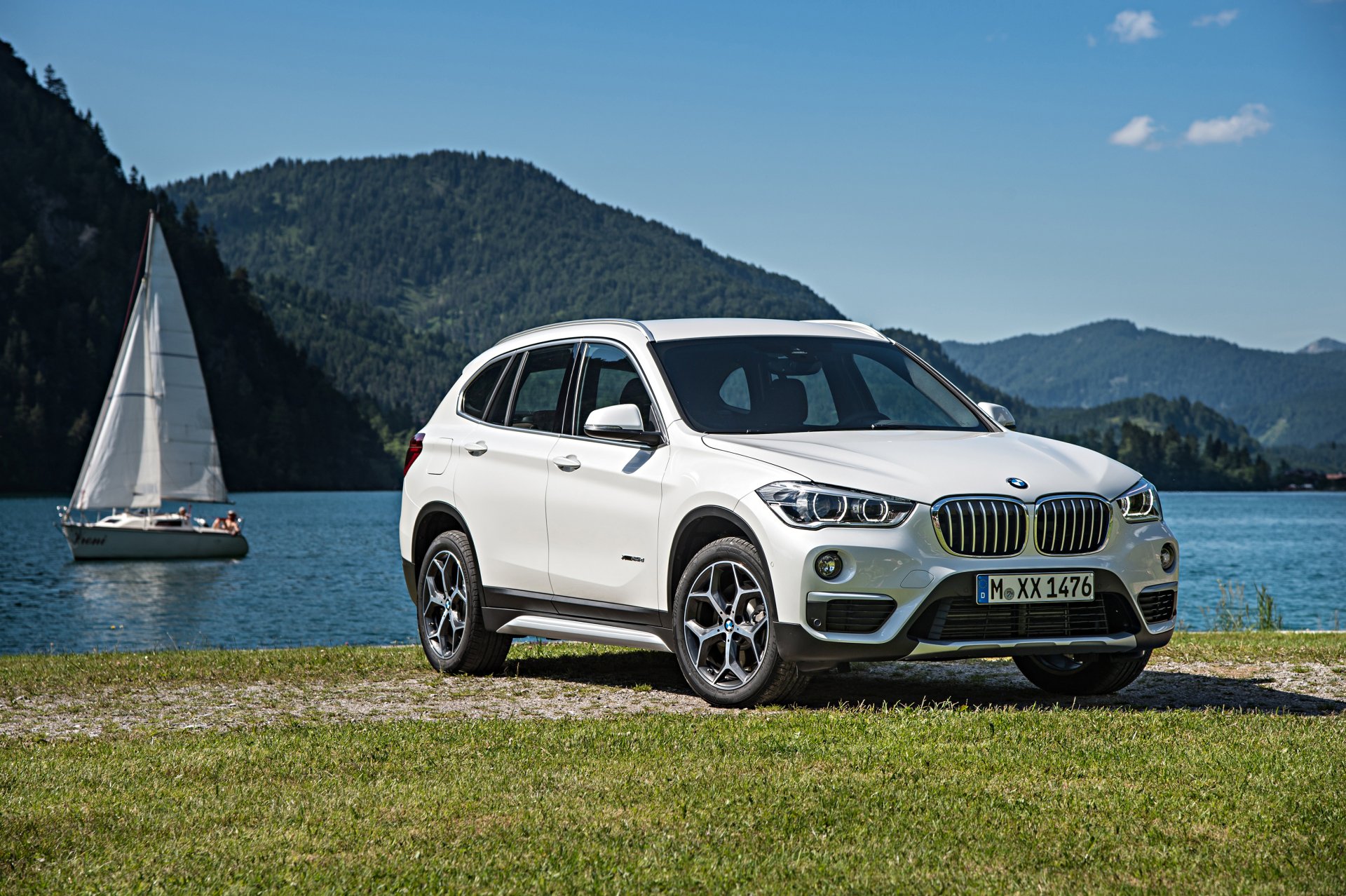 A white BMW X1 SUV parked by a lakeside with mountains in the background. 4K Ultra HD PC desktop wallpaper capturing the vehicle and serene nature scene.