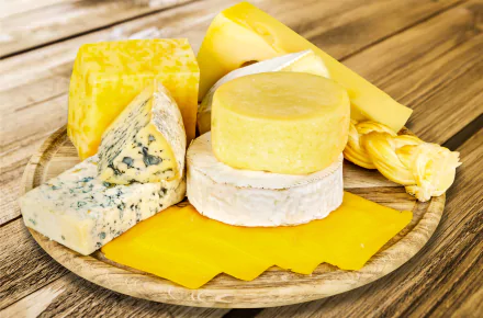 Assorted cheeses (brie, blue, cheddar, gouda) arranged on a wooden board — food, cheese; 5K Ultra HD PC desktop wallpaper background.
