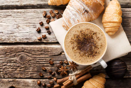4K Ultra HD wallpaper featuring a coffee cup sprinkled with cinnamon, surrounded by croissants, star anise, and coffee beans on a rustic wooden surface.