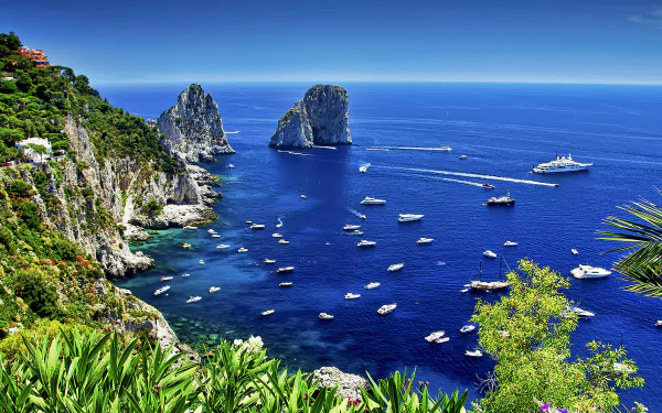 A stunning view of Capri, Italy, showcasing the vibrant blue sea with boats scattered across the water, framed by lush greenery and iconic rocky cliffs against a clear horizon.