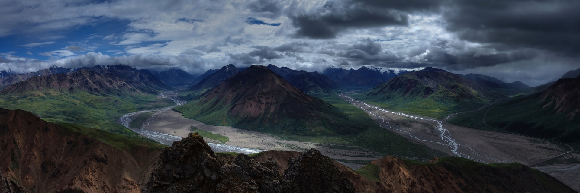 A 4K Ultra HD panorama of Denali National Park in Alaska showcasing mountains, a winding river through the valley, and dramatic cloud-filled skies.