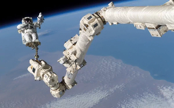 An astronaut operates a robotic arm in space, with Earth visible in the background. This HD desktop wallpaper captures a stunning moment of human ingenuity by NASA.