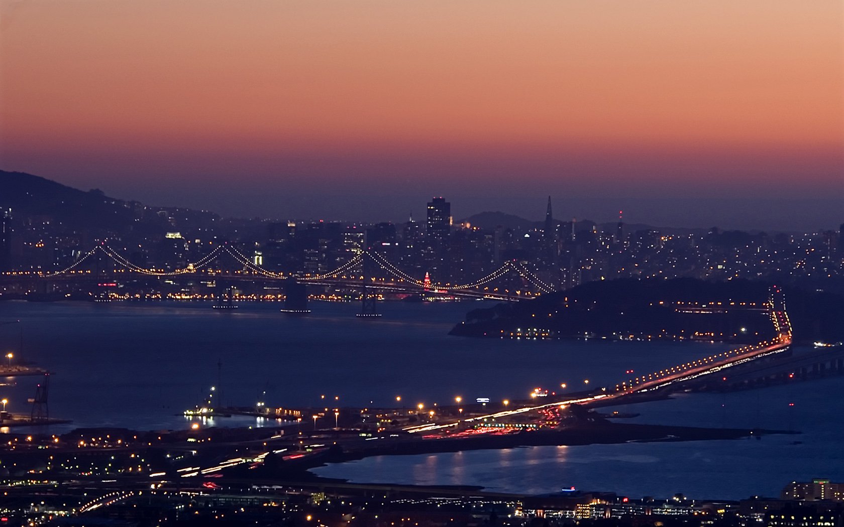 HD PC desktop wallpaper of San Francisco's man-made skyline and illuminated bridges stretching across the bay at dusk.