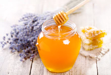 Close-up of a jar filled with honey, a honey dipper dripping honey into the jar, with lavender flowers and honeycomb in the background. 4K Ultra HD PC wallpaper.