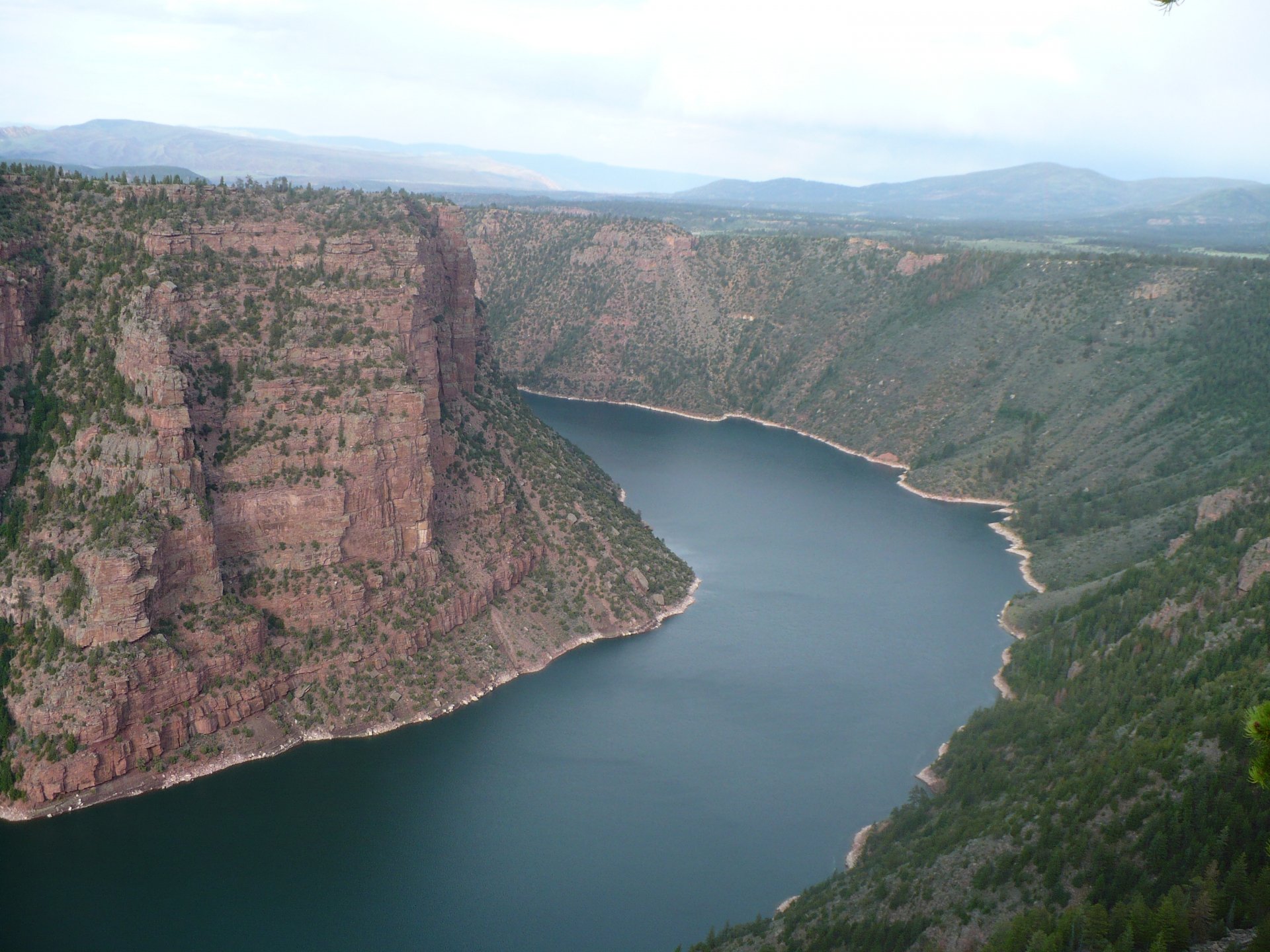 HD desktop wallpaper showcasing a vast canyon with steep rocky cliffs and a winding river below, surrounded by lush greenery under a cloudy sky.