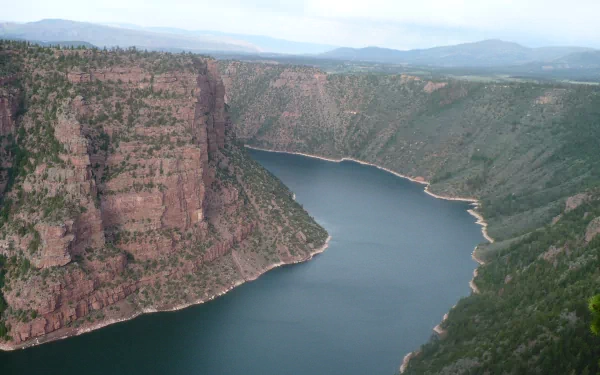 HD desktop wallpaper showcasing a vast canyon with steep rocky cliffs and a winding river below, surrounded by lush greenery under a cloudy sky.