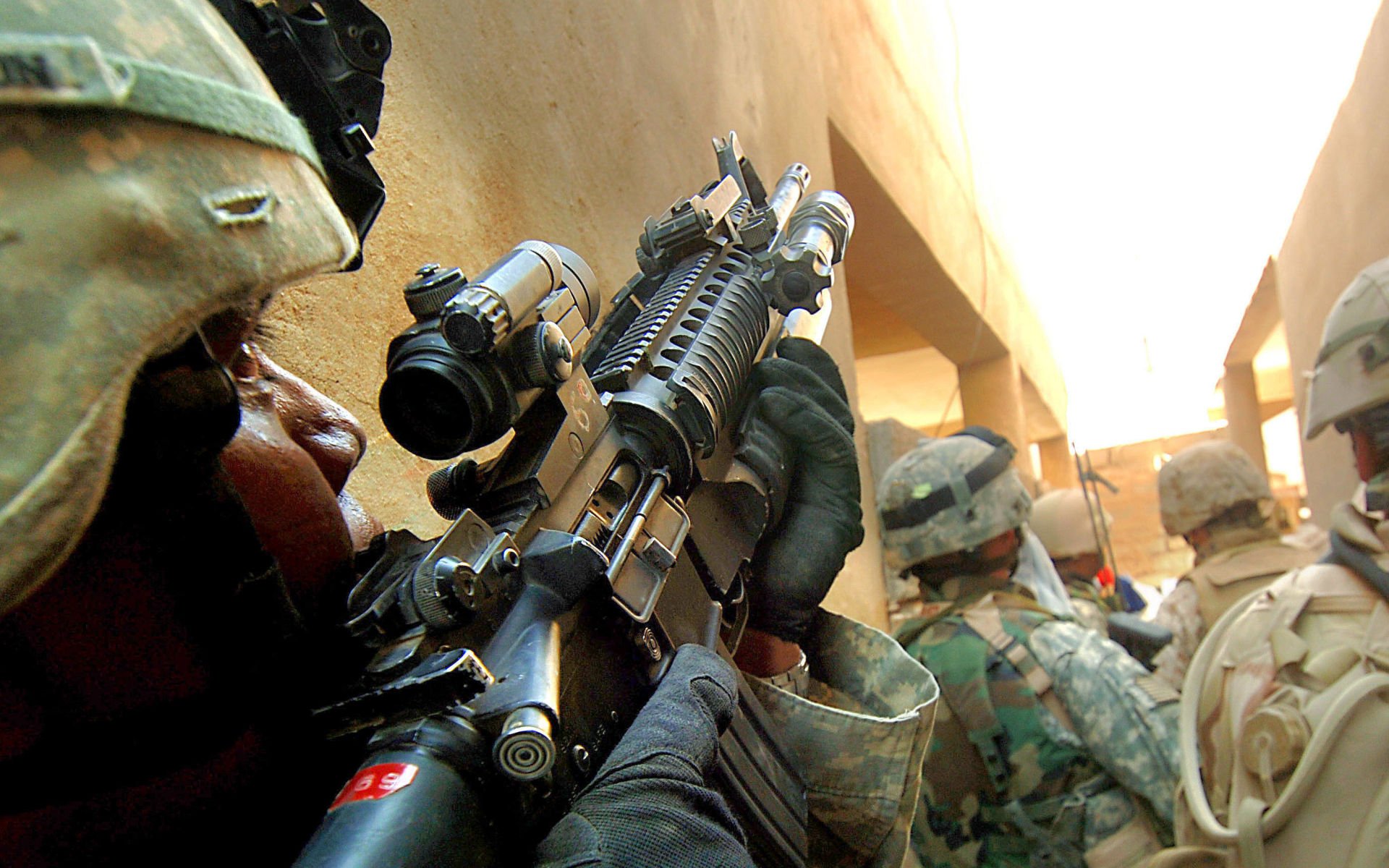 A soldier gripping an M4 Carbine in a narrow corridor, surrounded by fellow troops. This HD wallpaper captures the intensity of military operations in the United States Army.