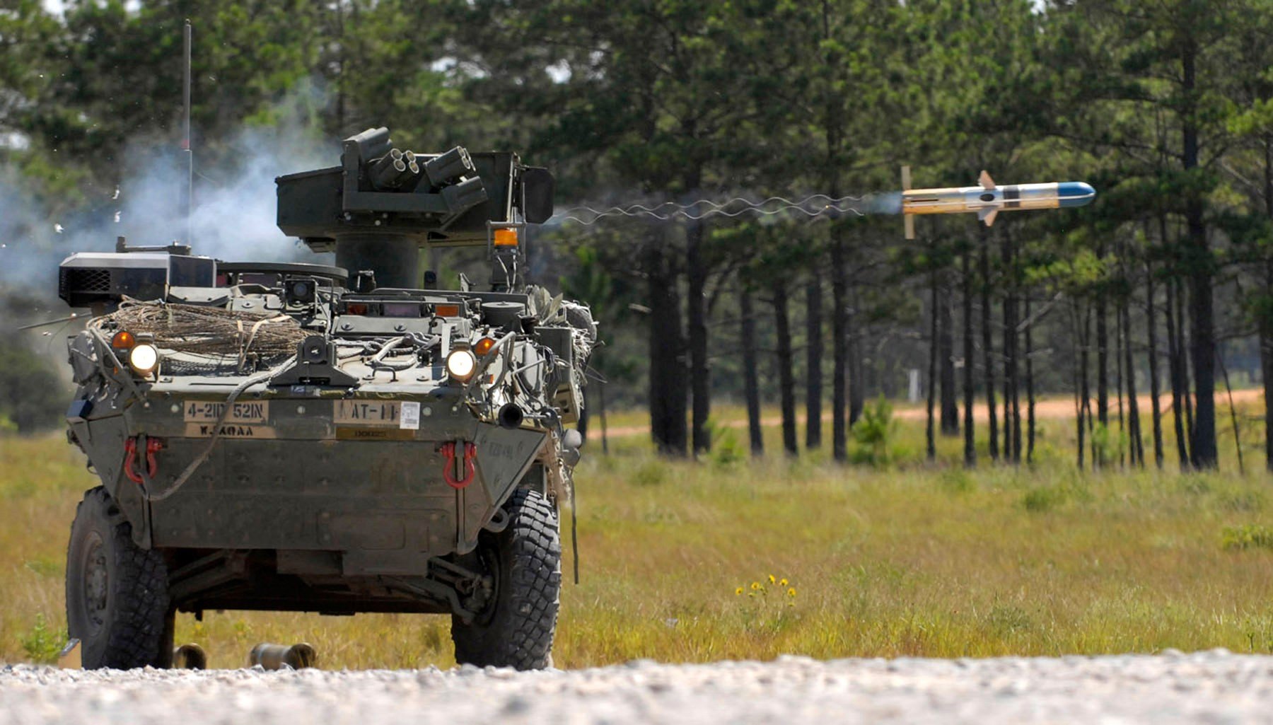 A military vehicle launches a missile in a dynamic outdoor setting, surrounded by dense trees. This HD desktop wallpaper captures an intense moment in military operations.