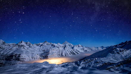 A breathtaking winter landscape featuring snow-covered mountains under a starry sky, with fog gently enveloping the valley, creating a serene night scene.