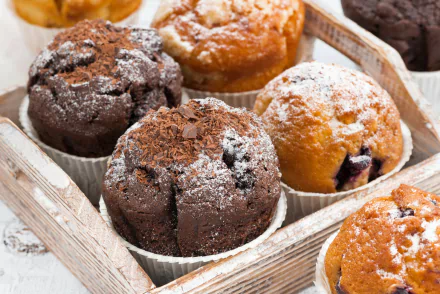 Close-up of assorted chocolate and fruit muffins dusted with powdered sugar, arranged in a rustic wooden tray, captured as an HD PC desktop wallpaper background.