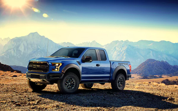 HD PC desktop wallpaper featuring a blue Ford F-150 Raptor truck parked on rugged terrain against a backdrop of mountains and clear sky.
