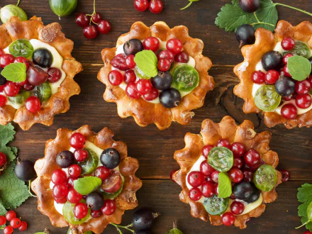 HD desktop wallpaper featuring sweet berry desserts with currants, grapes, and green leaves arranged on a wooden surface.