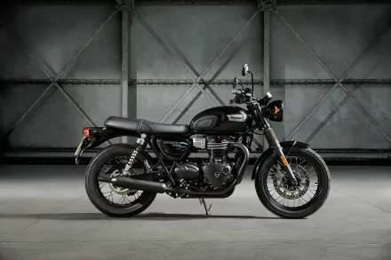 HD desktop wallpaper showcasing a sleek Triumph Bonneville T100 motorcycle in a dimly lit industrial setting.