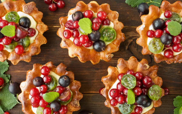 HD desktop wallpaper featuring sweet berry desserts with currants, grapes, and green leaves arranged on a wooden surface.