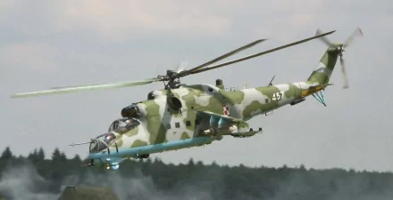 HD desktop wallpaper of a Mil Mi-24 helicopter in flight, showcasing its distinctive camouflage design against a blurred background of trees. Military aviation at its finest.