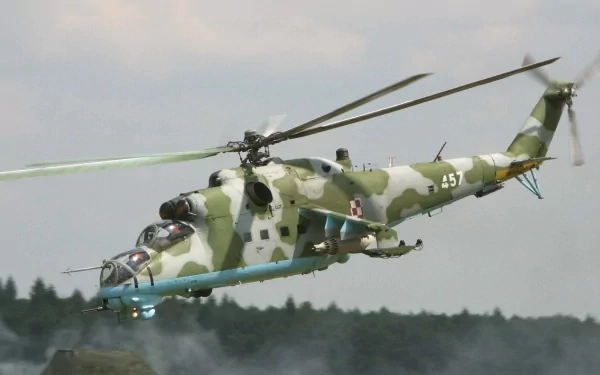 HD desktop wallpaper of a Mil Mi-24 helicopter in flight, showcasing its distinctive camouflage design against a blurred background of trees. Military aviation at its finest.