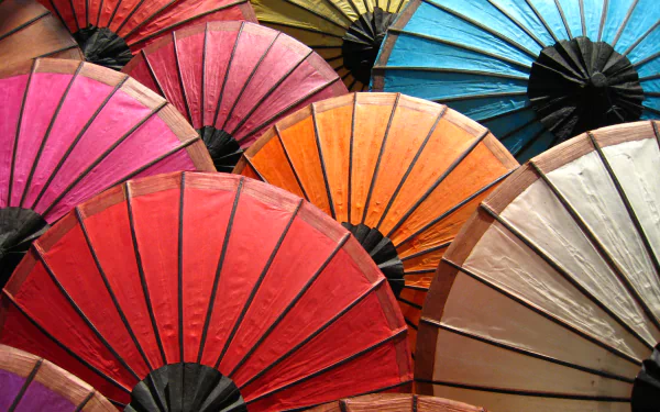 Vibrant overlapping paper parasols in red, pink, orange, blue and beige; colorful man-made umbrellas forming a decorative 2K Quad HD PC desktop wallpaper background.