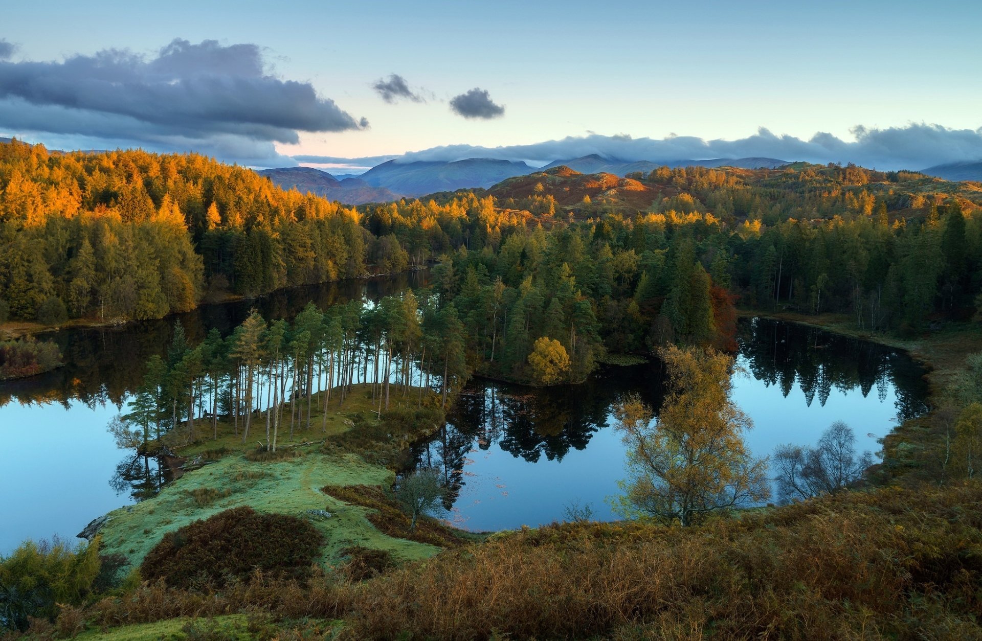 HD PC desktop wallpaper background: nature landscape of a forested lakeshore with trees and small islands reflected in calm water, rolling hills and a bright sky.