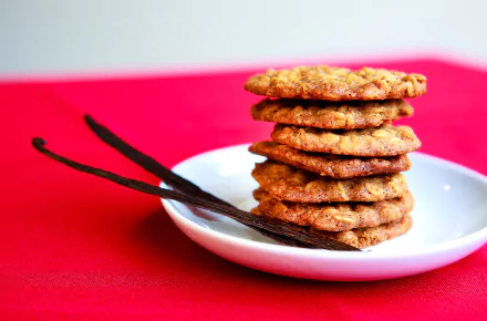 HD desktop wallpaper featuring a stack of golden vanilla cookies on a white plate with vanilla pods, set against a vibrant red background.