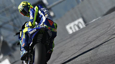 A high-definition desktop wallpaper featuring a MotoGP rider in full gear, captured during a high-speed race, with a focus on the dynamic motion and vibrant colors of the sport.