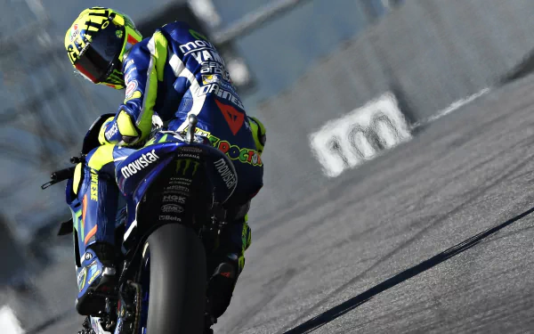 A high-definition desktop wallpaper featuring a MotoGP rider in full gear, captured during a high-speed race, with a focus on the dynamic motion and vibrant colors of the sport.