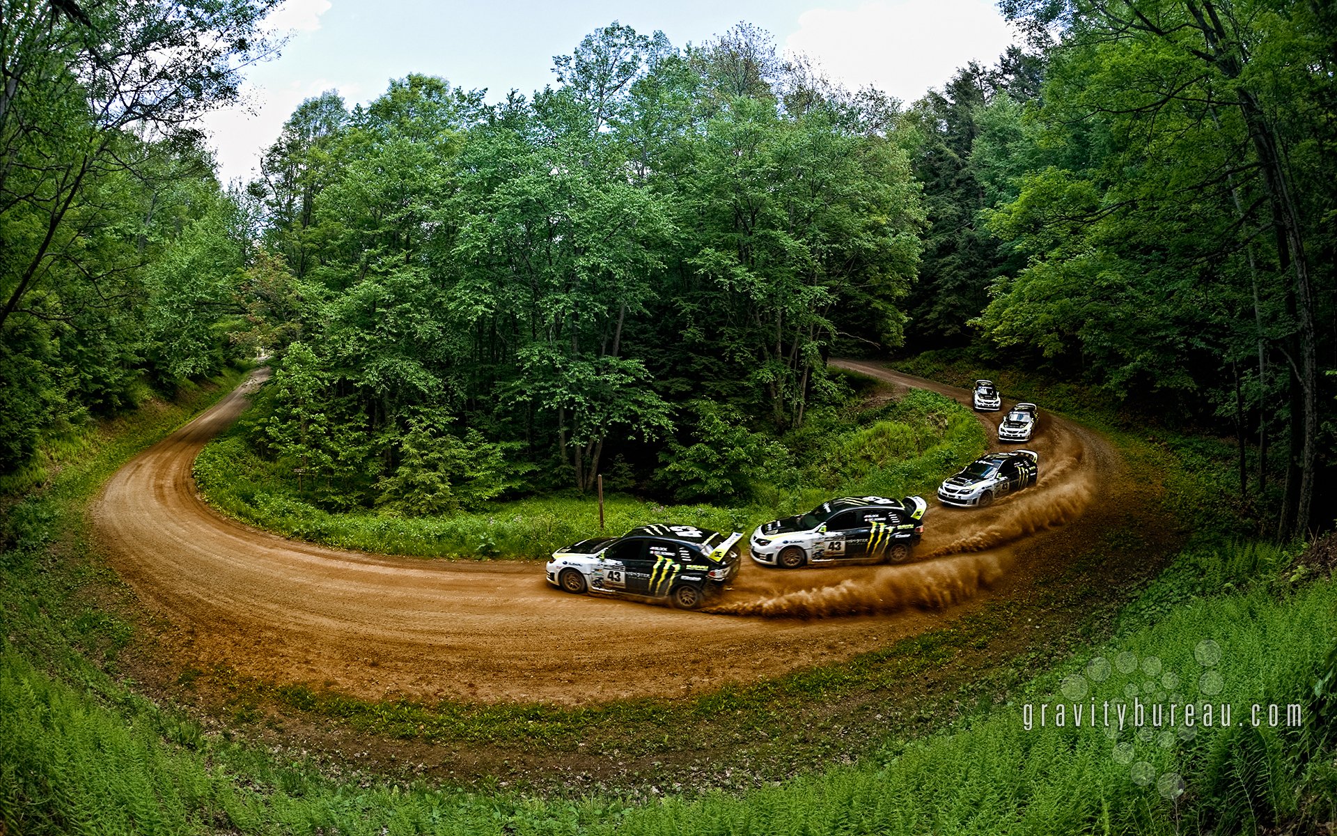 HD PC desktop wallpaper featuring a Subaru rallye vehicle drifting on a forested dirt road during a high-speed turn.