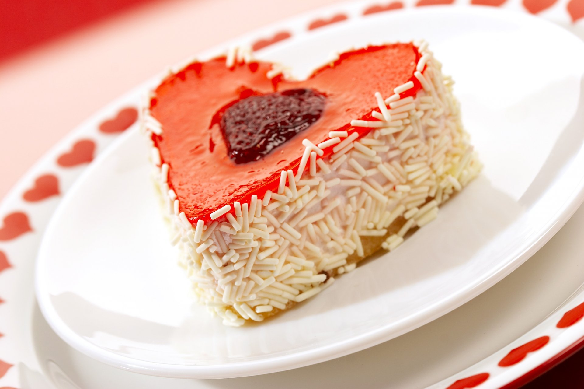 A heart-shaped dessert covered in sprinkles sits on a white plate adorned with red hearts, featured as a vibrant HD PC desktop wallpaper for food and sweets enthusiasts.