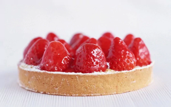 A close-up of a delicious strawberry tart, featuring glossy red strawberries atop a creamy filling and crust, serves as an enticing HD desktop wallpaper background for food lovers.
