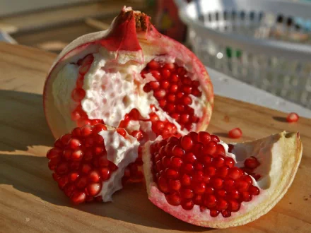 HD desktop wallpaper featuring a close-up of a fresh, opened pomegranate with vibrant red seeds on a wooden surface.