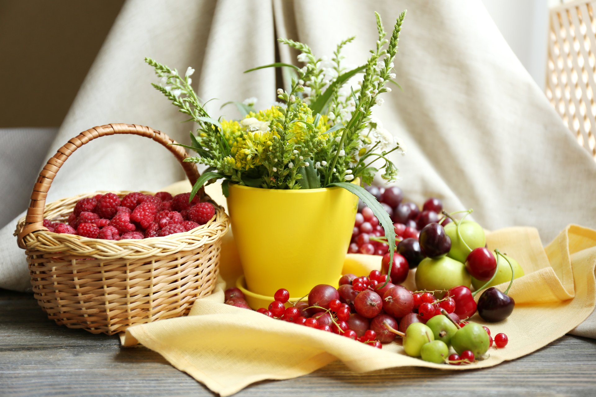 5K Ultra HD desktop wallpaper: still life of a wicker basket of raspberries, scattered cherries and gooseberries, and a yellow pot of green foliage on a draped cloth.