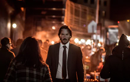 HD desktop wallpaper of Keanu Reeves as John Wick in a scene from John Wick: Chapter 2, showcasing him walking through a dimly lit, crowded urban area.