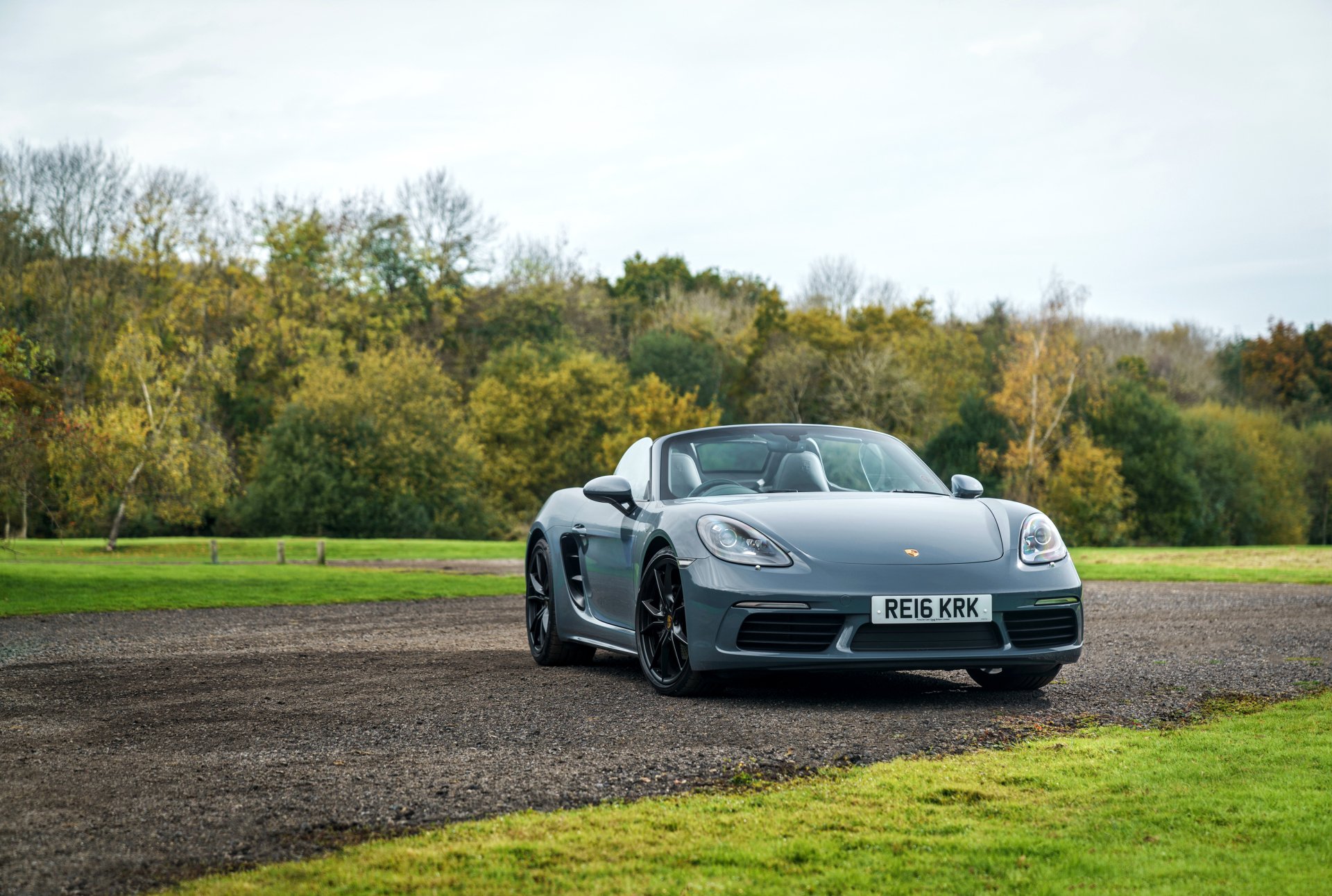 Silver Porsche Boxster parked on a gravel path with autumn trees in the background, captured in HD as a PC desktop wallpaper and background.