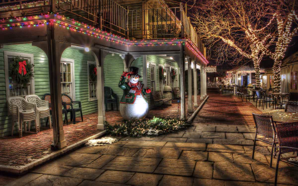 Christmas-themed 4K Ultra HD desktop wallpaper featuring a festive, warmly lit porch with holiday decorations and a snowman statue along a quiet, tree-lined street.