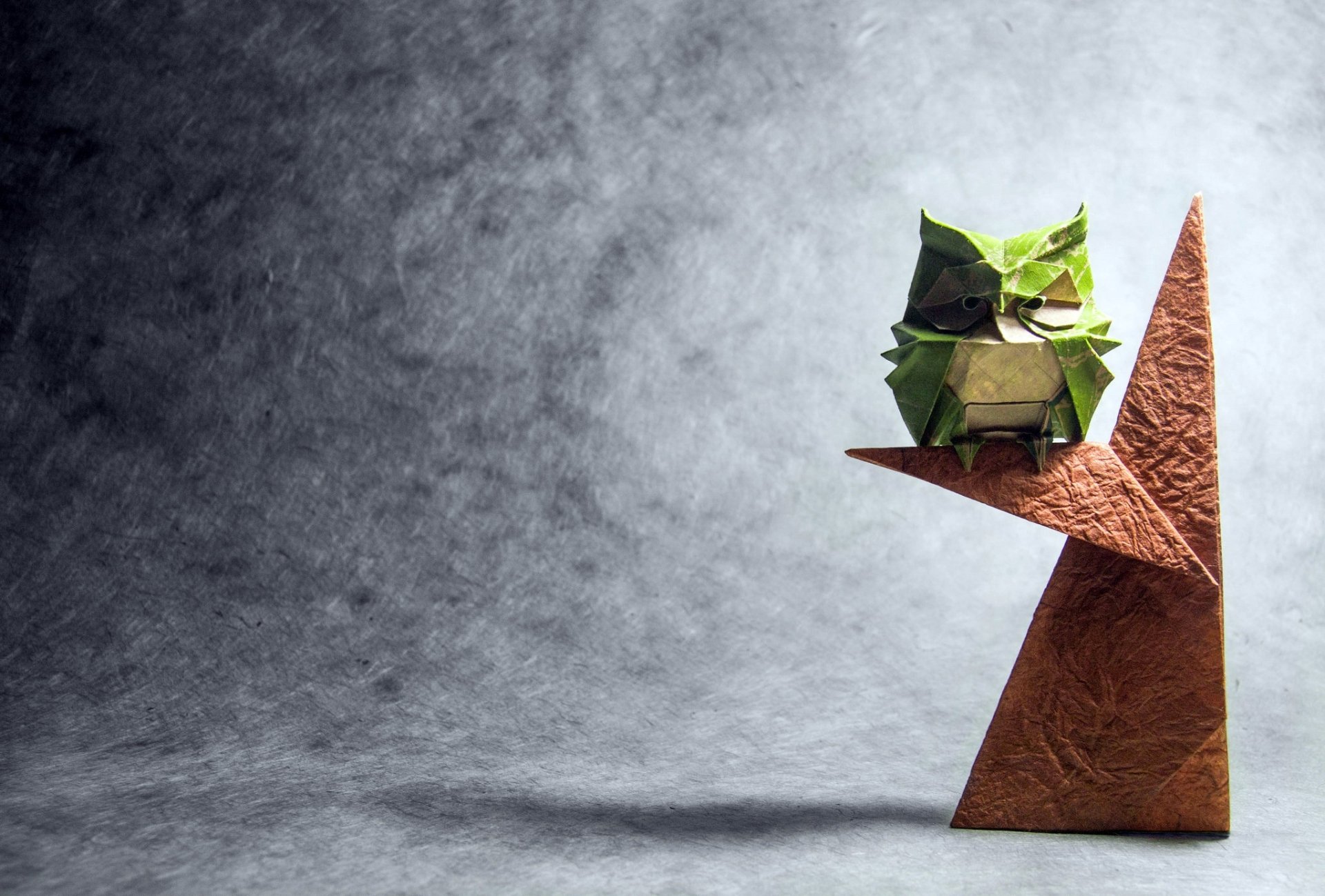 HD desktop wallpaper featuring a man-made origami owl perched on a geometric shape against a textured grey background.