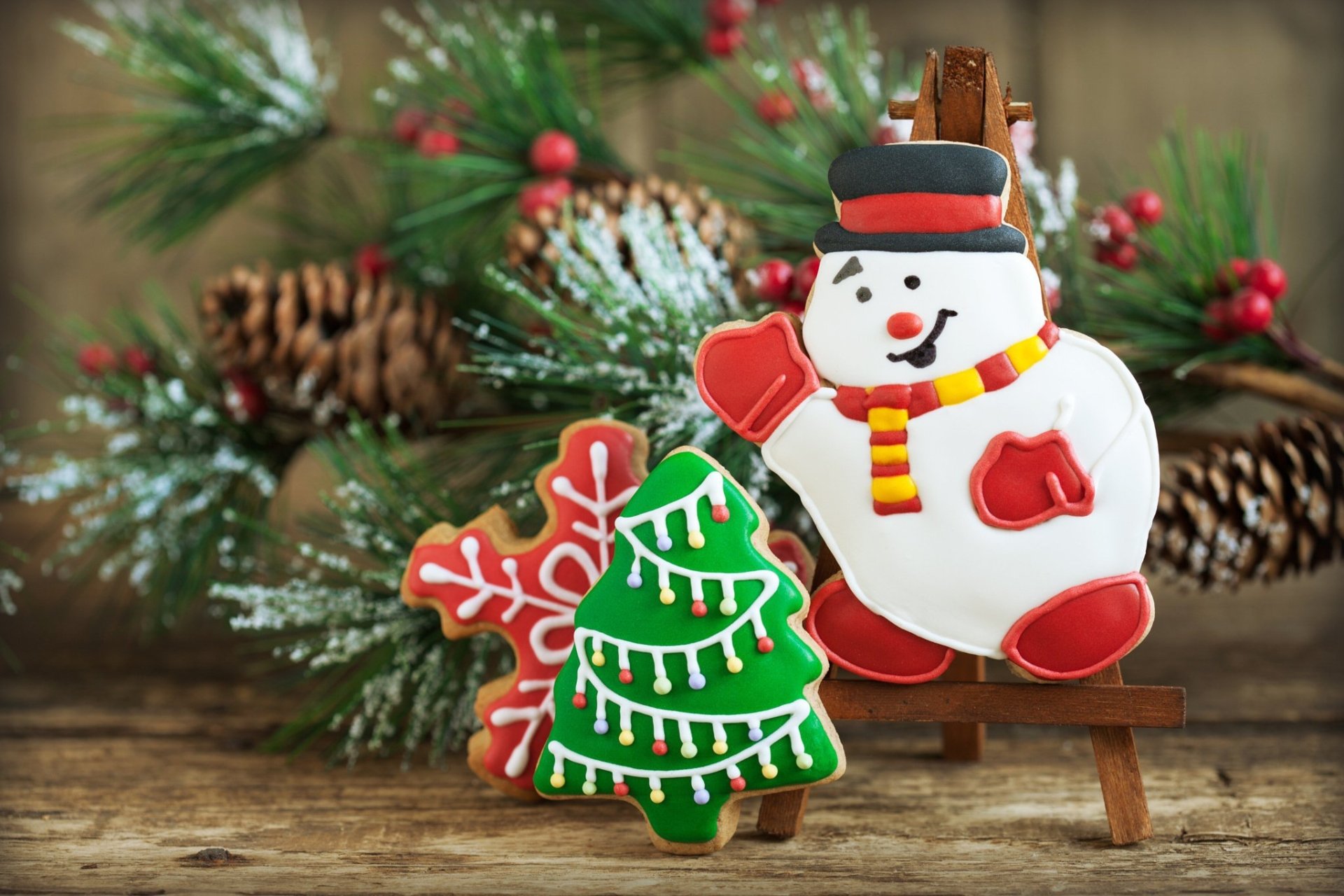 HD PC desktop wallpaper featuring festive Christmas holiday cookies shaped like a snowman, Christmas tree, and snowflake, with pinecones and greenery in the background.