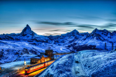 HD desktop wallpaper showing a scenic winter view of the Matterhorn in the Swiss Alps. A train glows warmly as it travels through the snowy landscape at dawn or dusk.