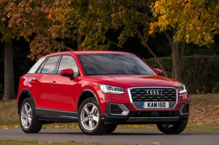 Red Audi Q2 SUV parked by autumn trees — 2K Quad HD PC desktop wallpaper/background showing the car in a front three-quarter view.