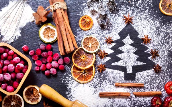 A festive HD desktop wallpaper featuring star anise, cinnamon sticks, dried orange slices, red berries, and a powdered Christmas tree on a dark surface, creating a vibrant and warm still life.
