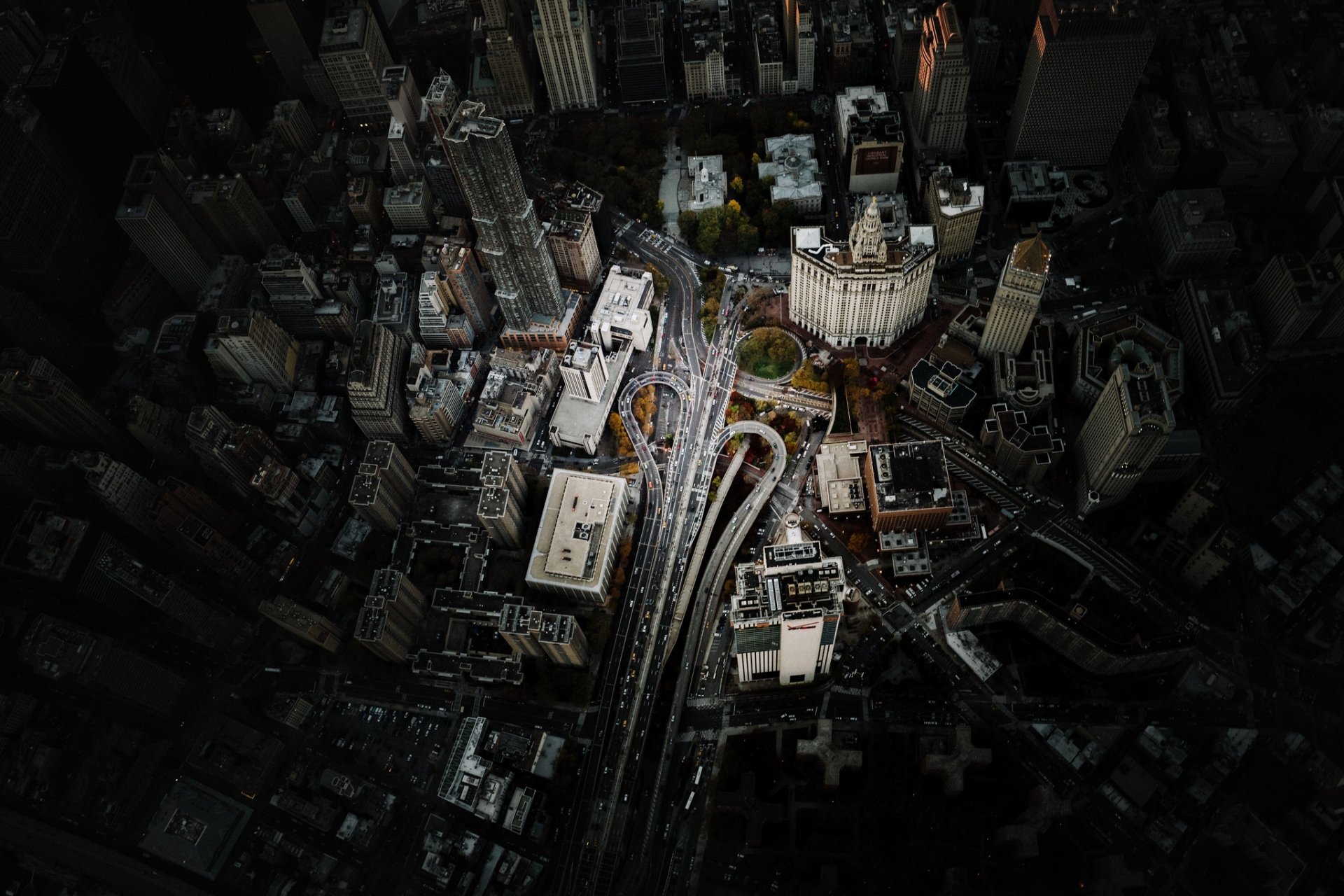 Aerial view of Manhattan, New York City featuring roads, tall buildings, and urban landscapes under a shadowy, dramatic light. HD desktop wallpaper and background.