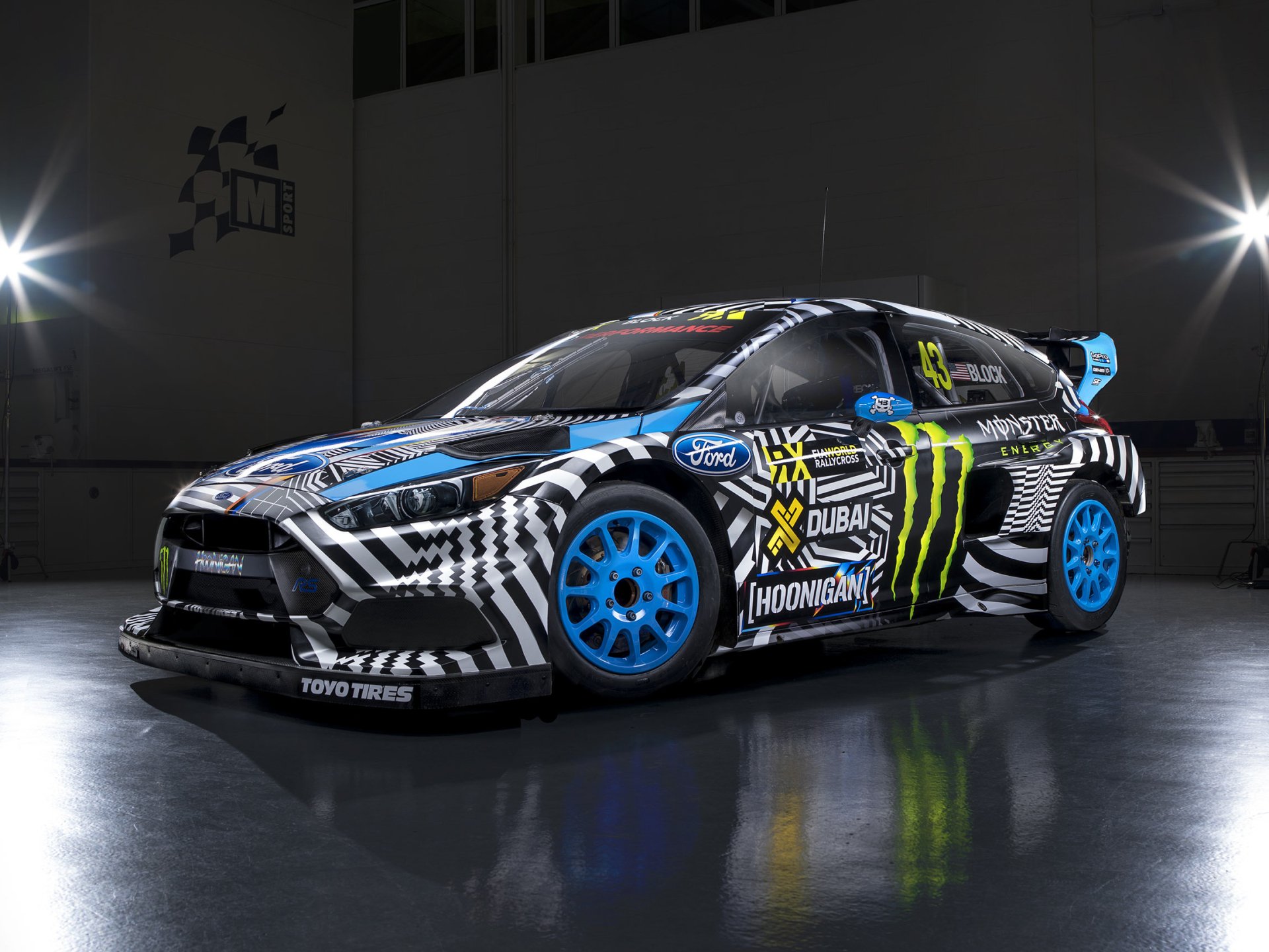 HD desktop wallpaper featuring a race-ready Ford Focus RS with bold black, white, and blue livery, adorned with sponsor decals including Monster and Hoonigan.
