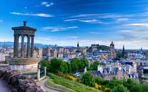 Panoramic 4K Ultra HD view of Edinburgh's cityscape in Scotland, featuring historic buildings and monuments under a vibrant blue sky.