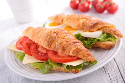 A 4K Ultra HD desktop wallpaper featuring fresh croissant sandwiches with lettuce, tomato, sliced egg, and cheese on a white plate, accompanied by cherry tomatoes.