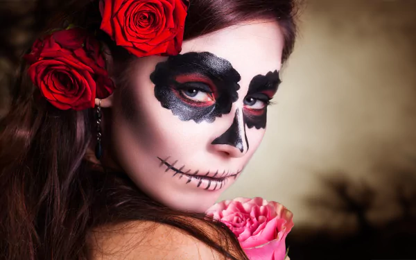 A brunette with blue eyes and Day of the Dead sugar skull makeup holds a red rose, offering an artistic and striking HD desktop wallpaper background.