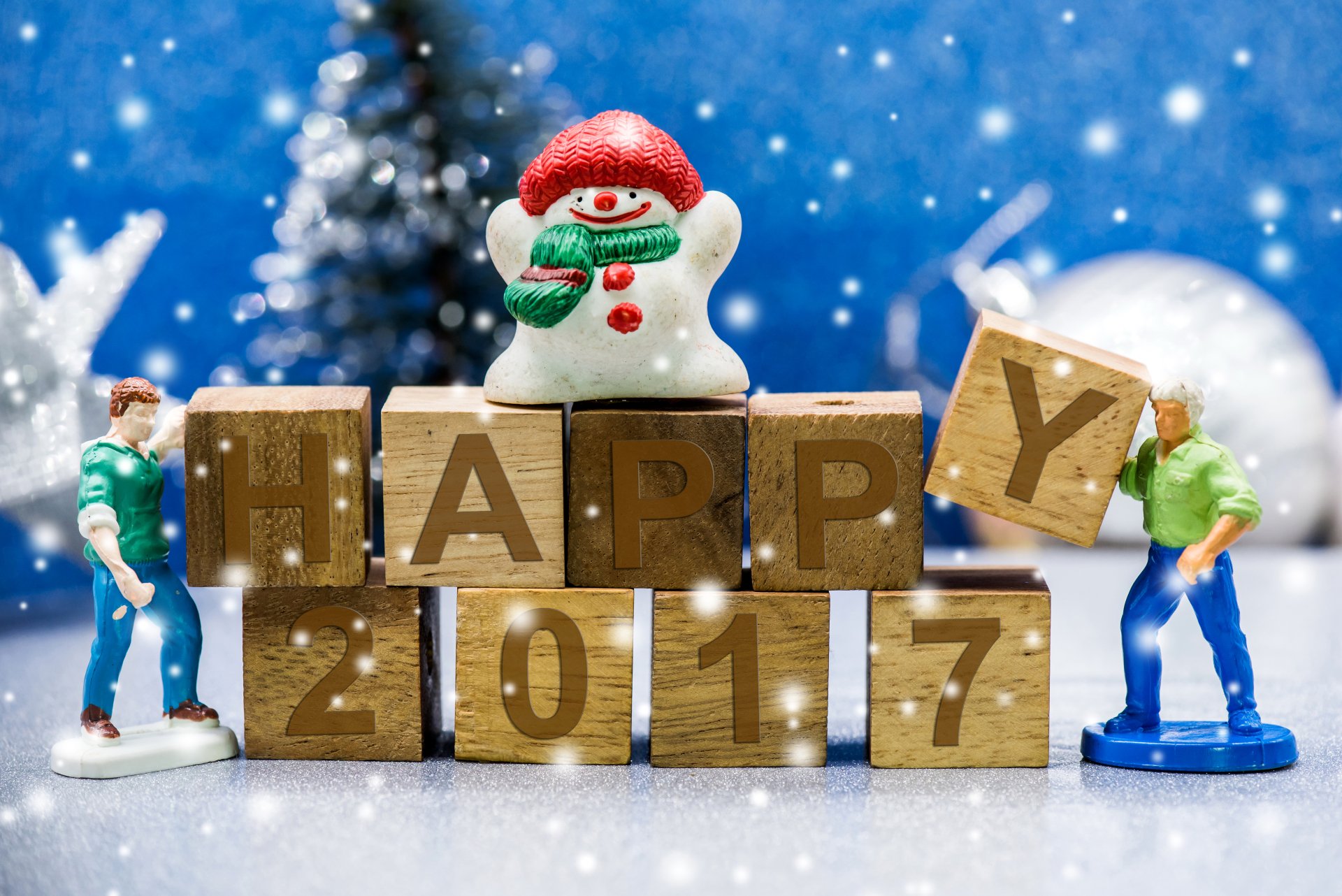 Festive New Year 2017 holiday 8K Ultra HD PC wallpaper: toy snowman and miniature figures with wooden blocks spelling HAPPY 2017 against a snowy blue bokeh background.