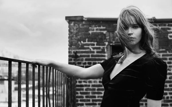 Black-and-white HD PC desktop wallpaper: moody rooftop portrait of a poised woman in a dark dress leaning on a railing against a brick wall.