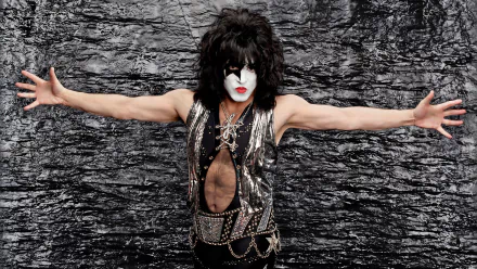 A high-definition wallpaper featuring a member of KISS in full glam metal attire and makeup, posing with arms outstretched against a textured black and silver background.